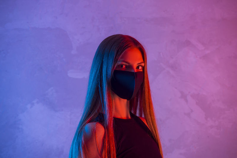 Portrait of woman wearing mask standing against colored background