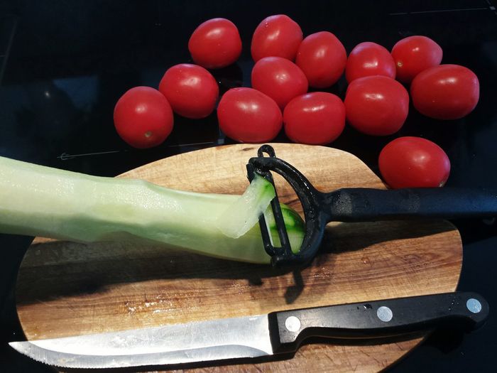 Cucumber and tomatoes by peeler and kitchen knife on table