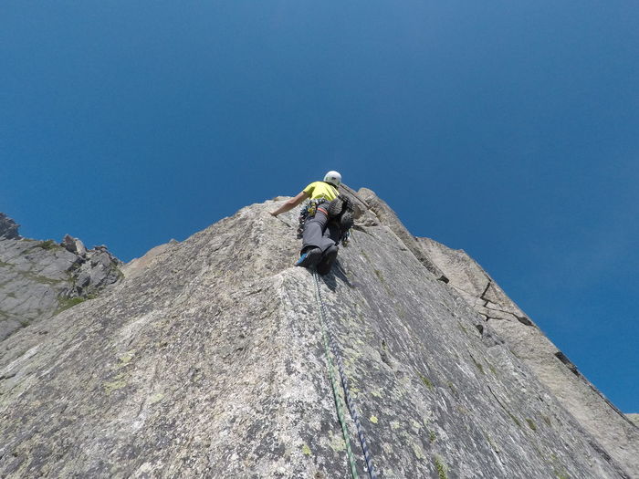 Low angle view of man on rock climbing against clear blue sky