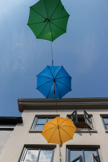 Low angle view of umbrella's against building and blue sky 
