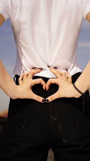 Midsection rear view of woman making heart shape with fingers on back