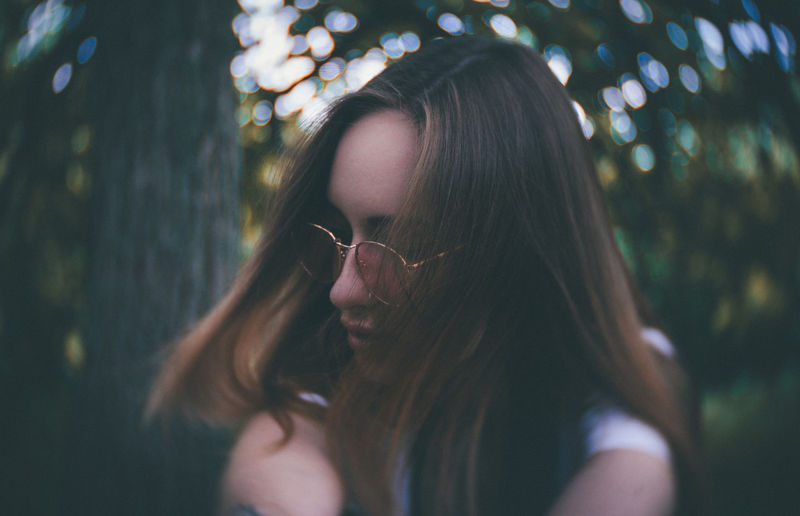 Adult Beautiful Woman Brown Hair Close-up Contemplation Dreamy Focus On Foreground Glasses Hair Hairstyle Headshot Leisure Activity Lifestyles Long Hair One Person Outdoors Plant Portrait Real People Tree Women Young Adult Young Women