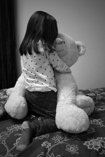 Rear view of girl playing with teddy bear on bed at home