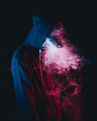 Man exhaling smoke while standing in darkroom
