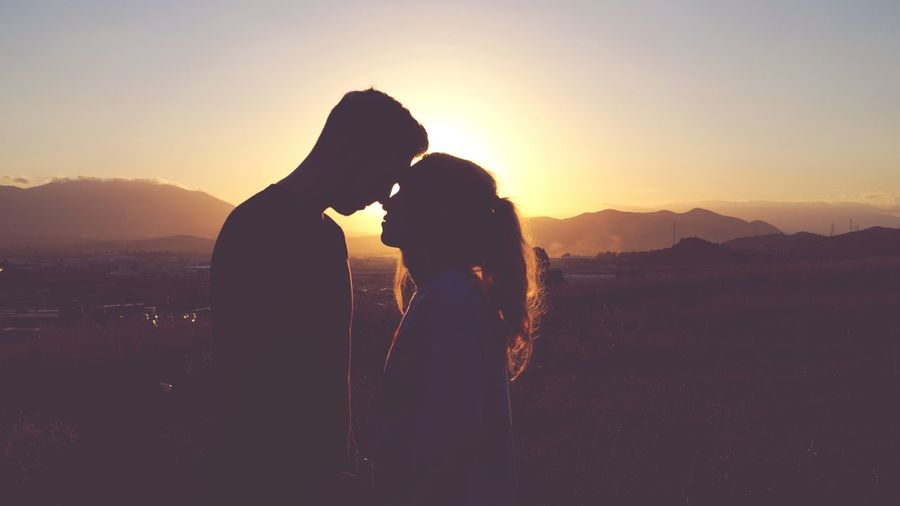 Silhouette couple romancing against sky during sunset