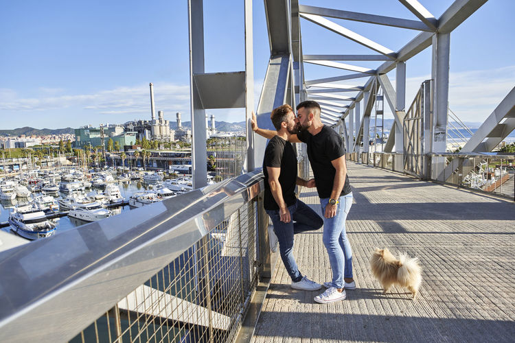 Affectionate gay couple kissing on footbridge during sunny day