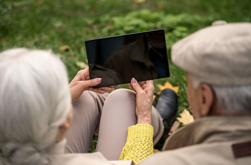 Rear view of senior couple holding digital tablet sitting at park