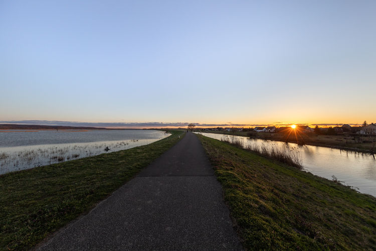 Road by river against clear sky during sunset