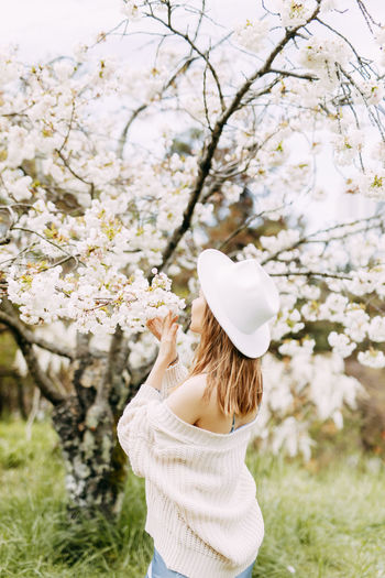Gentle girl in a dress and a fashionable hat is walking enjoying the smell of flowers in the park