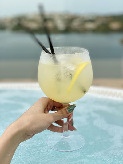 Cropped image of hand holding drink at swimming pool