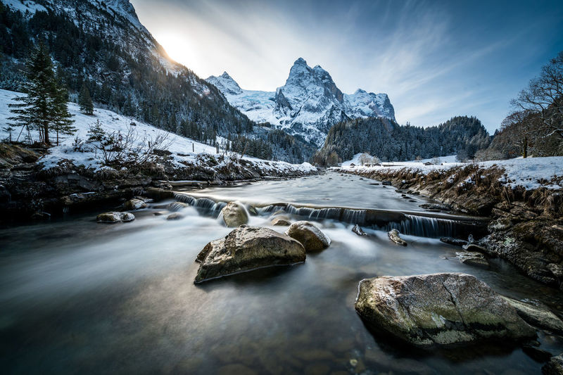 Scenic view of stream by snowcapped mountains against sky
