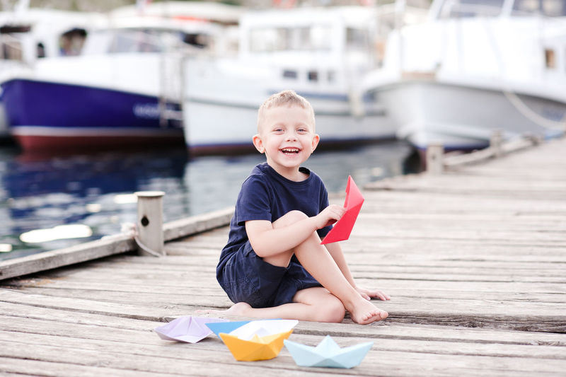 Smiling kid boy 5 year old playing with paper boats over sea background. laughing child outdoors.