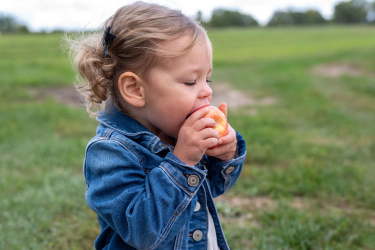 Cute girl eating apple standing on field
