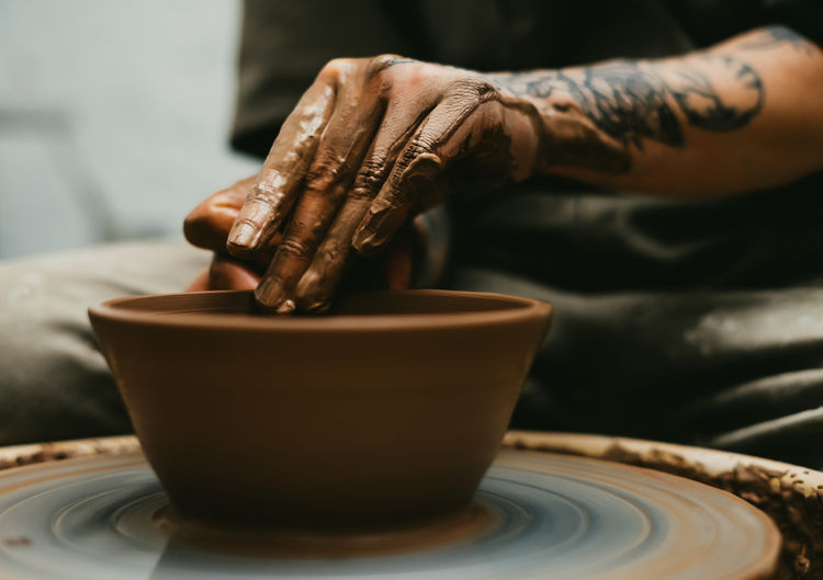 Closeup of dirty hands of anonymous craftsman using pottery wheel and making clay pot in workshop