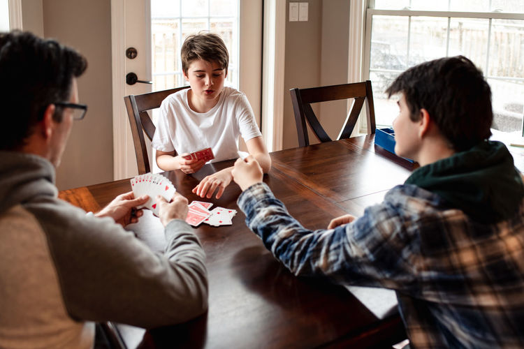 Father and adolescent sons playing cards at the table together.