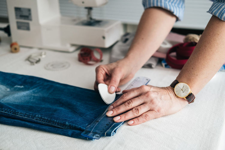 Cropped hands of tailor marking jeans with chalk on table in workshop