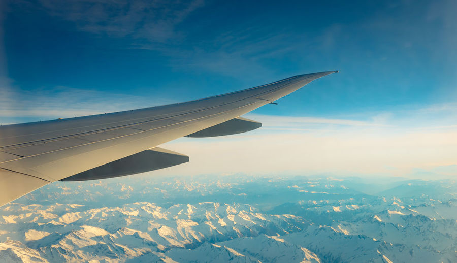 Wing of plane over mountain cover with white snow. airplane flying on blue sky. scenic view.