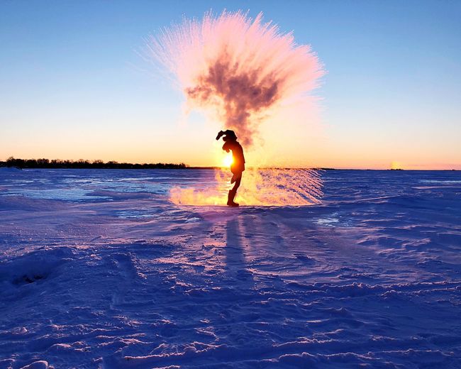 Silhouette person throwing snow on field against sky during sunset
