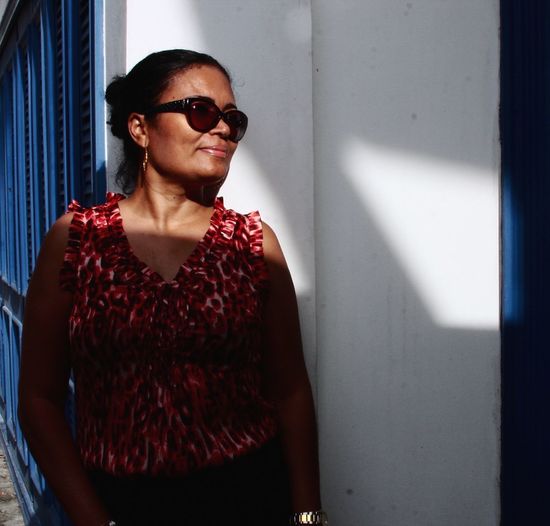 Woman wearing sunglasses while standing against wall