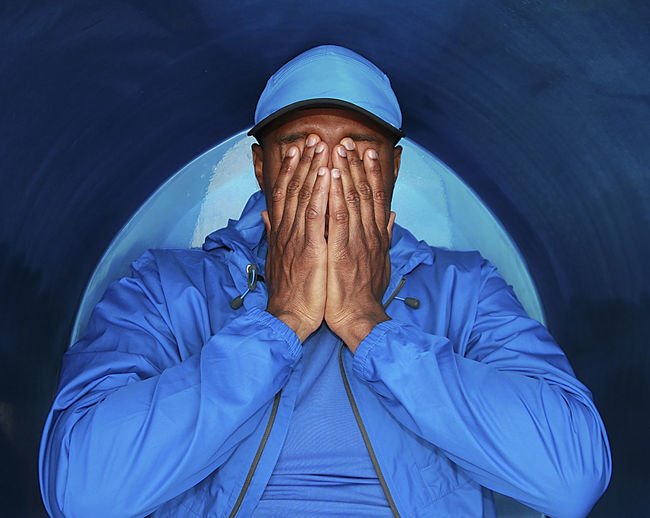 Man covering face against blue wall