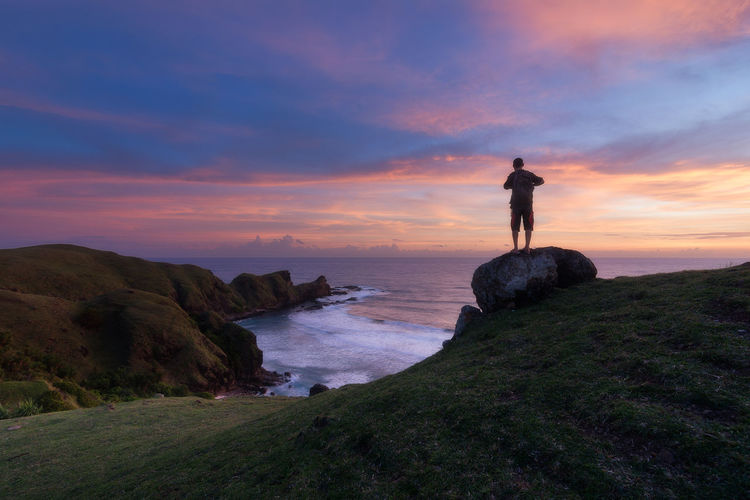 Man standing on beach cliff during sunset