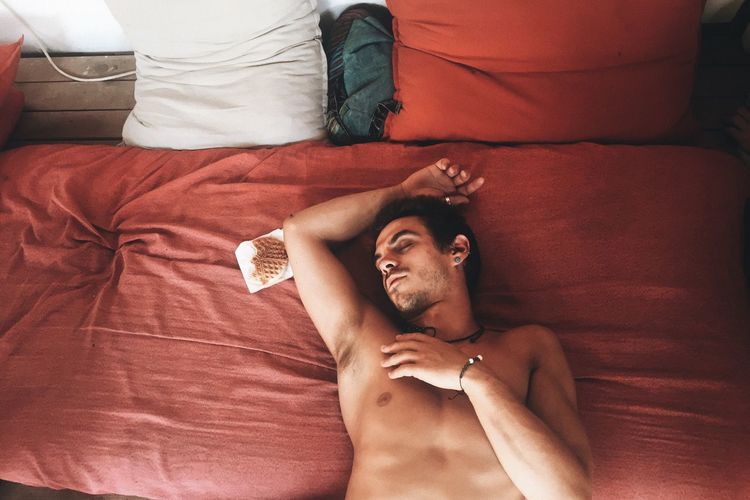 Full length of shirtless man lying on bed