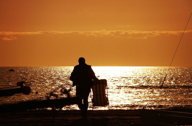 Silhouette man on beach against sky during sunset