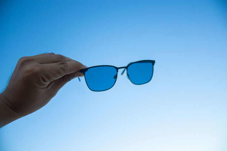 Cropped image of hand holding sunglasses against clear blue sky