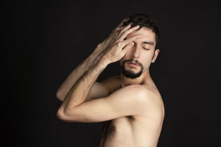 Portrait of shirtless young man against black background