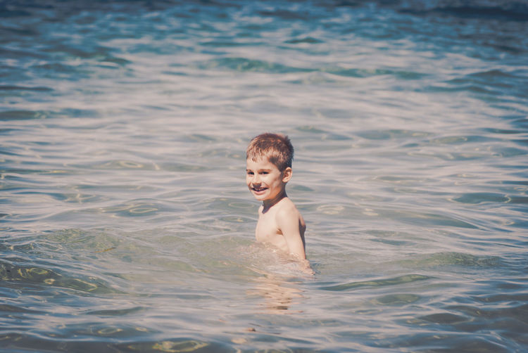 Portrait of smiling boy playing in sea on sunny day