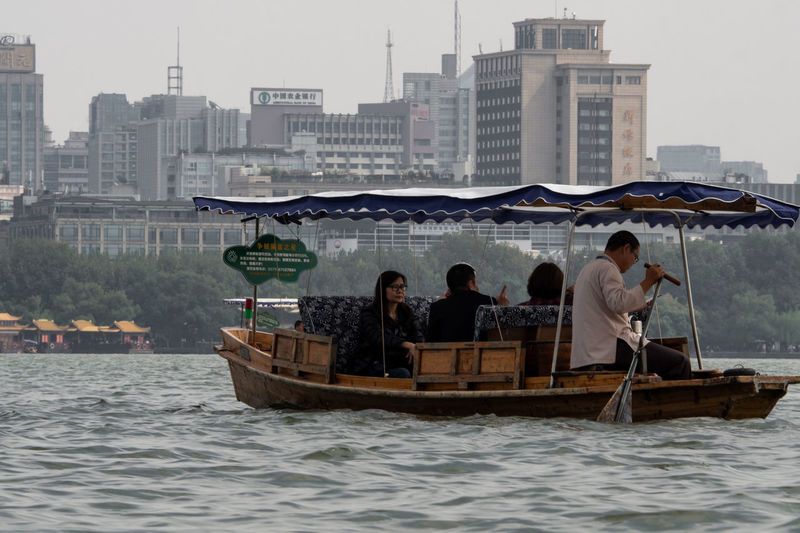 People on boat in river against cityscape