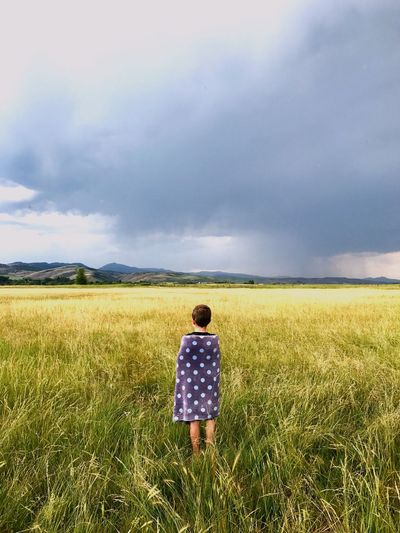 Rear view of boy standing on grassy field against cloudy sky