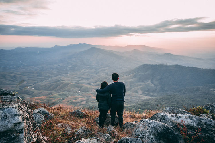 Rear view of couple looking at mountains against sky during sunset