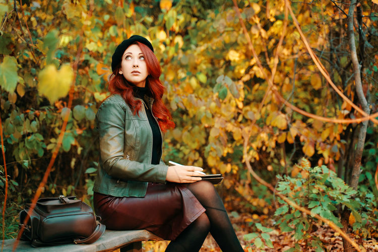 Young woman looking away while sitting on tree during autumn