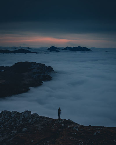 Man standing on rock against sky during sunset