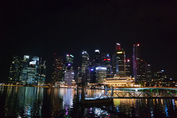 Pier over sea against illuminated buildings in city