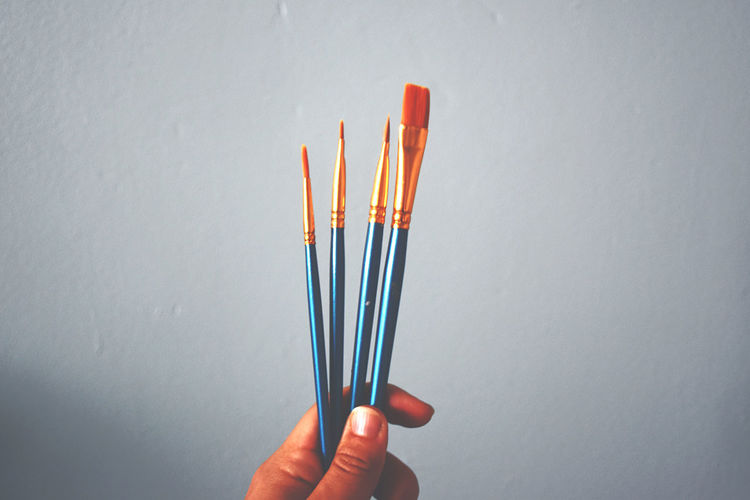 Close-up of hand holding paint brushes against white background