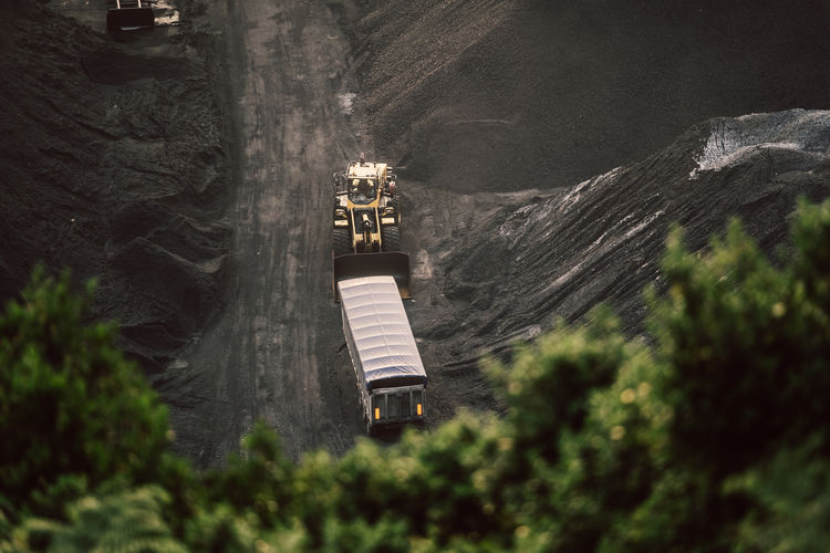 Aerial view of modern loader transporting cargo along coal mining stock in daylight