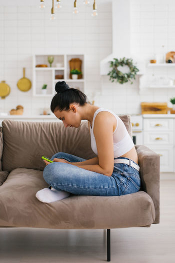 Young woman holds a smartphone in her hands, hunched over sitting on the couch