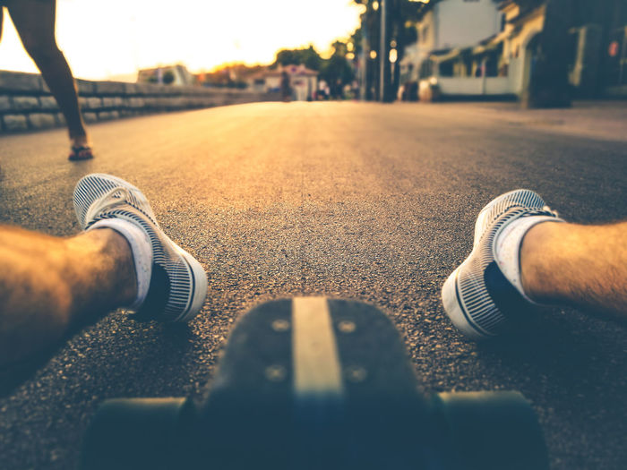 Low section of man sitting with skateboard on road