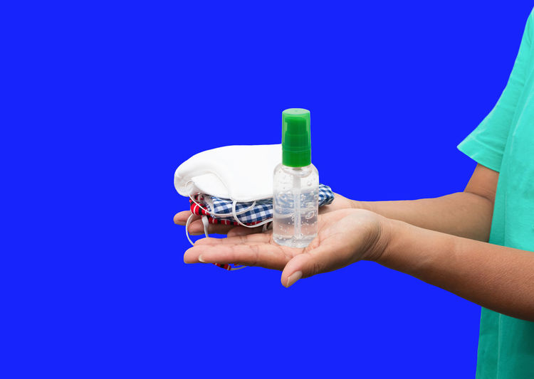 Close-up of hand holding bottle against blue background