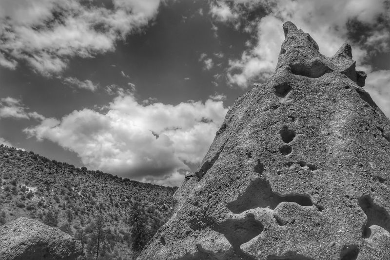 Black and white landscape of clouds, hill and pointed rock formation in bandelier national monument