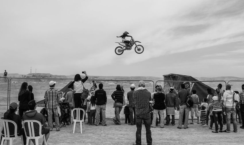 People watching at motorcyclist performing stunt against sky