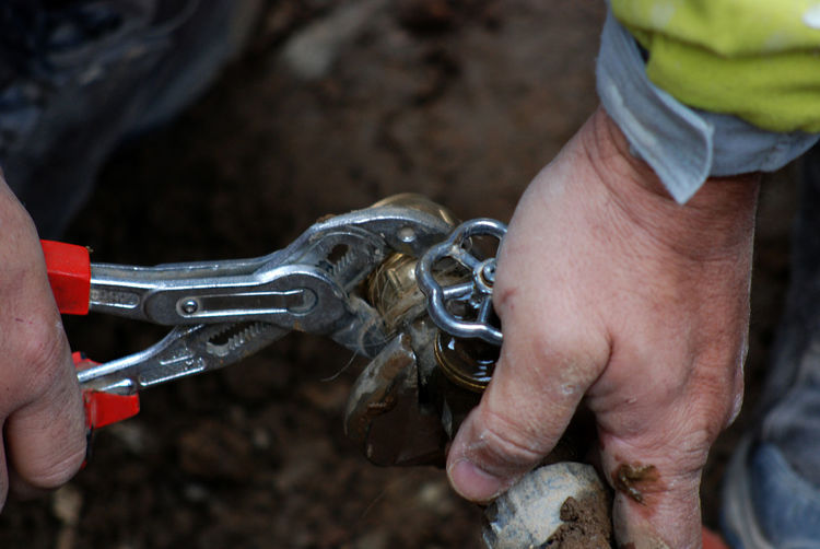 Cropped hands using pliers on pipe at field