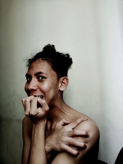 Portrait of shirtless young man biting nails against wall