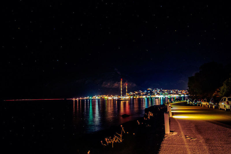 Illuminated city by sea against sky at night