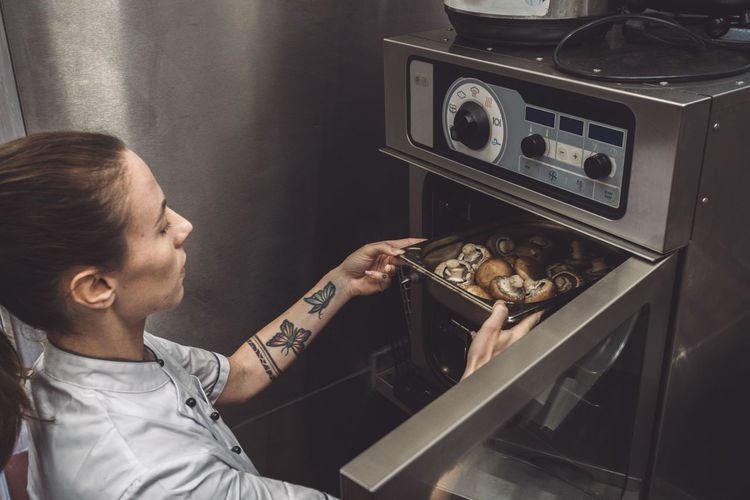 High angle view of female chef baking mushrooms in oven