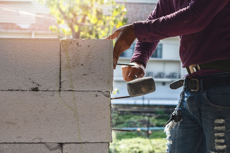 Midsection of man hammering stone wall at construction site