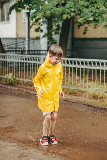 A boy in a yellow raincoat walks outside in the rain. a child jumps on the narrows. 