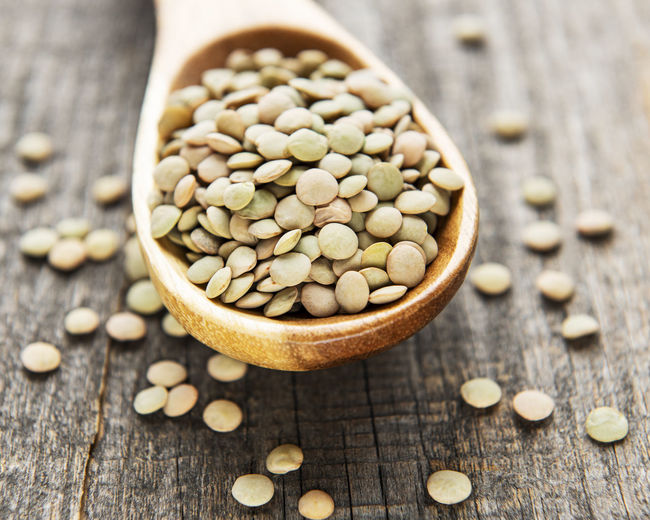 Pile of raw lentil in a spoon on old wooden background